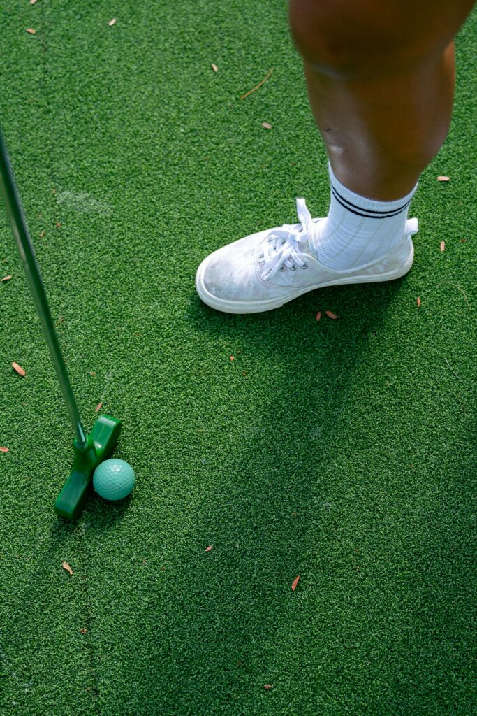 A golfer preparing to putt on green artificial turf with a turquoise golf ball.